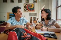 Photo of two students smiling and doing schoolwork.